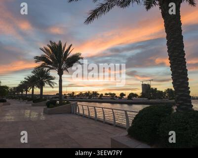 Die Szene fängt einen ruhigen Sonnenuntergang am Al Raha Beach in Abu Dhabi mit Palmen an der Uferpromenade ein. Sanfte Pastellfarben füllen die SK Stockfoto