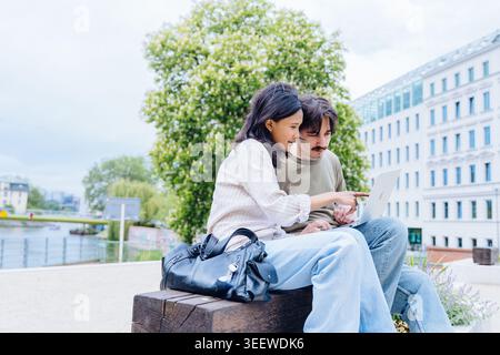 Multikulturelles Paar mit Laptop auf der Bank im modernen europäischen Park Stockfoto
