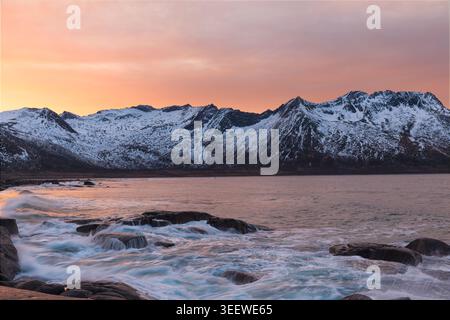 Meereswellen bei Sonnenuntergang mit schneebedeckten Bergen Stockfoto