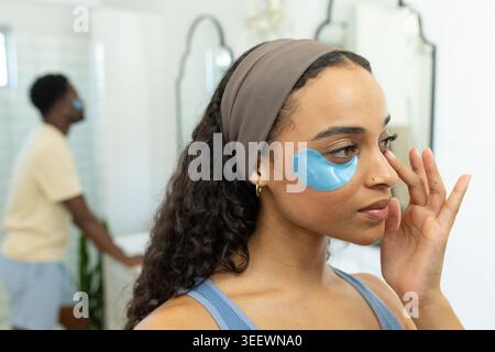 Afroamerikanisches Paar, das blaue Hydrogel-Flecken unter den Augen am Waschtisch im Bad aufträgt, Kopierraum Stockfoto