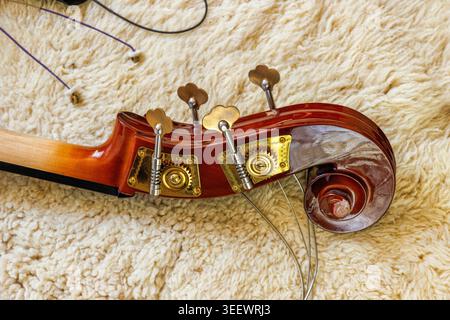 Nahaufnahme einer Kontrabass-Rolle mit Messingklammern und losen Saiten auf einem Wollteppich aus Lammfell. Kopierbereich Stockfoto