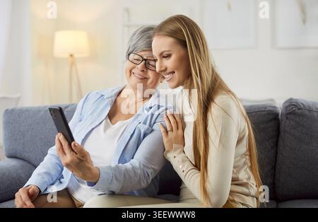 Eine junge Erwachsene Frau bringt ihrer älteren Mutter den Umgang mit moderner Technologie bei Stockfoto