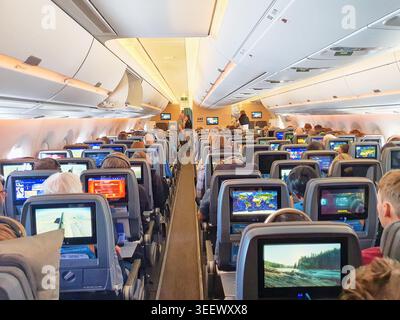 Das Innere einer Kabine eines Verkehrsflugzeugs zeigt Economy-Class-Sitzplätze. Mehrere Reihen grauer Sitze sind mit individuellen Touchscreens ausgestattet Stockfoto