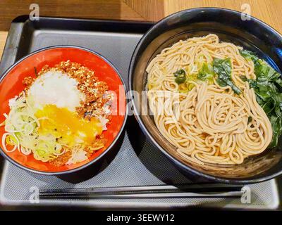 Eine Ansicht von oben auf ein traditionelles japanisches Essen, das auf einem schwarzen Cafeteria-Teller serviert wird. Links enthält eine lebhaft rote Schüssel ein Reisgericht, das mit dem Stockfoto