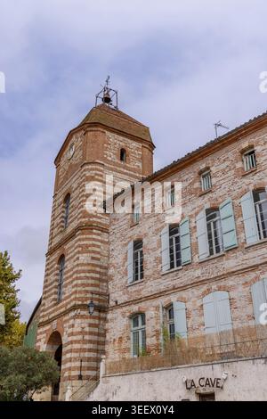 Alter Uhrenturm mit gestreifter Fassade neben dem traditionellen Gebäude mit blauen Fensterläden Stockfoto