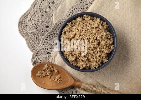 Gekochte Quinoa in einer grauen Keramikschale und auf einem Holzlöffel auf einer Leinentischdecke Stockfoto