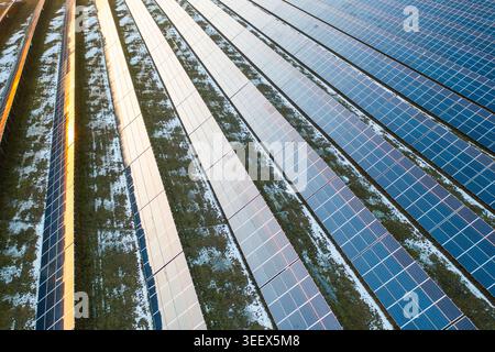 Photovoltaik-Solarpaneele, die in einem Stromerzeugungsbetrieb installiert sind, absorbieren Sonnenlicht für die Stromerzeugung. Die Tafeln sind in Reihen angeordnet, mit grünem Gras und etwas Schnee zwischen ihnen. Stockfoto