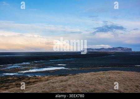 Riesige vulkanische Landschaft mit schwarzen Sandebenen und fernen Bergen unter einem bewölkten Himmel in Island Stockfoto