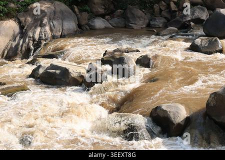 Schlammwasser fließt gewaltig über große Felsen- und Felsformationen und erzeugt einen wilden, chaotischen Fluss, der sich kraftvoll gefährlich und ungefährlich anfühlt Stockfoto