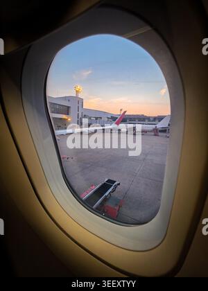 Blick aus dem Flugzeugfenster zeigt den Rollflugzeugflügel des Flughafenterminals während des ruhigen Abendhimmels, der auf den Reiseverkehr vorausschaut Stockfoto
