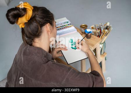 Konzentrierte Künstlerin, die Fähigkeiten in der neuen Aquarelltechnik übt, Zeichnen im Skizzenalbum. Stockfoto