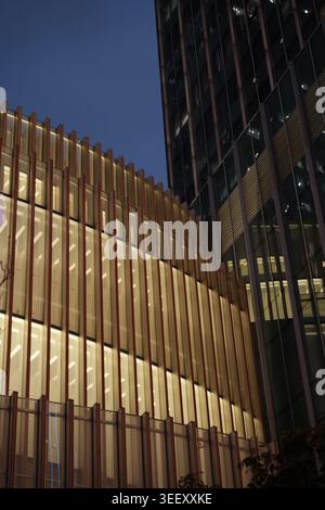 Niedrigwinkelaufnahme moderner Wolkenkratzer mit goldener, geschwungener Architektur, beleuchteten Bürofenstern vor tiefem, blauem Himmel Stockfoto