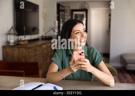 Frau sitzt am Tisch im Wohnzimmer und hält Smartphone Stockfoto