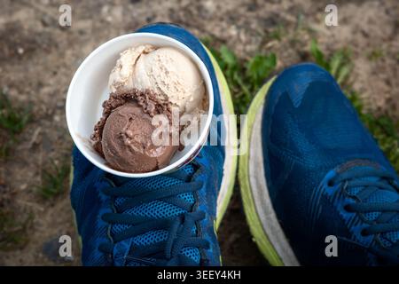 Zwei Kugeln Eis in einer Tasse, die auf einem Schuh ausgewogen ist, symbolisieren Desserts zum Mitnehmen, urbane Sommeratmosphäre, Kreativität und lustige Street Food-Konzepte. Stockfoto