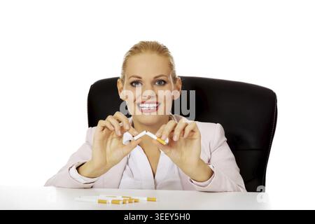 Lächelnde Geschäftsfrau, die hinter dem Schreibtisch sitzt und Zigaretten bricht Stockfoto