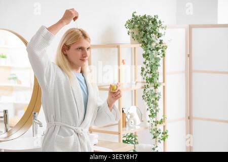 Junger blonder Mann, der Haarserum im Badezimmer aufträgt Stockfoto