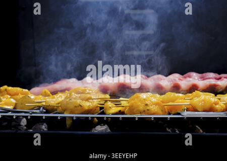 Marinierte Hähnchenspieße und rohe Rippchen, die auf einem heißen Grill kochen, erzeugen Rauch und ein köstliches Aroma Stockfoto