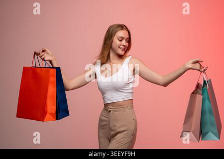Junge Frau, die gerne shoppt, bunte Taschen hält, glücklich mit Einkäufen, Einzelhandelstherapie und Konsumkonzept ist Stockfoto