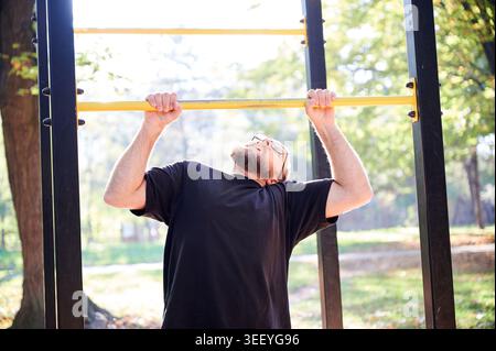 Der Mann führt an der horizontalen Bar im Outdoor-Fitnessstudio im Park Pull-Up aus. Aktive Fitnessszene für Krafttraining, Calisthenics, gesunden Lebensstil, sportliche Motivation oder Trainingsförderung Stockfoto