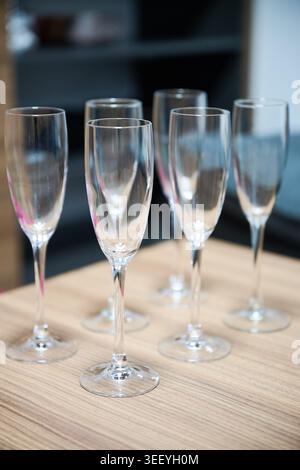Sektflöten auf Holztisch in moderner Innenausstattung. Nahaufnahme eleganter Stängelgläser für Sekt, Feier, Gastfreundschaft und festliches Getränkeservice-Konzept Stockfoto