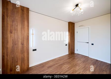 Helles Apartmentzimmer mit Designer-Beleuchtung, Holzelementen und glatten weißen Wänden. Minimales Wohn- oder Schlafzimmerinnere, Immobilien und modernes Komfortkonzept Stockfoto