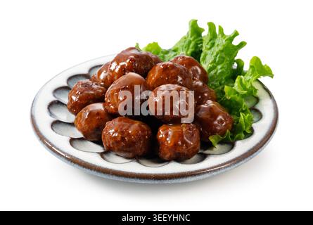 Japanische Fleischbällchen mit glänzender Teriyaki-Sauce und Salat auf einer Keramikplatte, isoliert auf weißem Hintergrund Stockfoto
