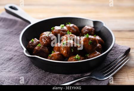Fleischbällchen mit glänzender Teriyaki-Glasur und gehackter Petersilie in einer gusseisernen Pfanne auf einem rustikalen Holztisch Stockfoto