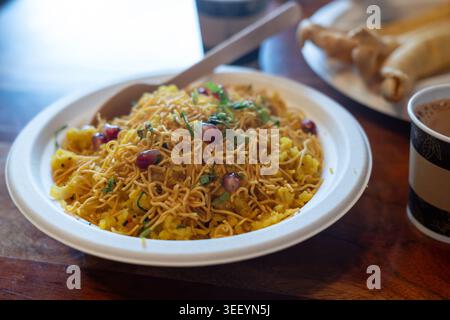 Poha indisches Frühstück aus nächster Nähe. Gesunde Pohe Reisflocken Gericht mit Tee auf verschwommenem Hintergrund Stockfoto