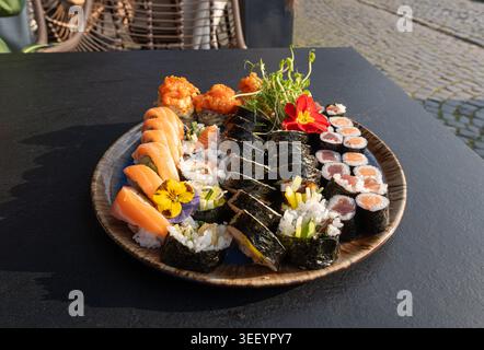 Buntes japanisches Sushi-Set mit verschiedenen Rollen und essbaren Blumen, verschiedene Sushi-Platten mit Lachs, Tempura und frischen Garnelen auf schwarzem Tablet Stockfoto