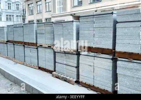 Große Stapel von Granitpflasterplatten befinden sich auf Holzpaletten auf der städtischen Straßenbaustelle. Granitpflasterplatten, Steinpflasterinstallation, Schüttgut Stockfoto
