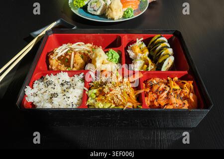 Japanisches Mittagessen in Bento Box mit frittierten Tintenfischringen, Sushi-Rolls, Salat, Reis, eingelegtem Ingwer und Wasabi, Fisch Maki Rolls, japanischen Meeresfrüchten, asiatischen Di Stockfoto