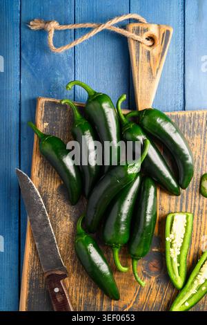 Jalapeno-Paprika mit Schnitten auf Schneidebrett und Messer auf blauem Holztisch. Frisches, scharfes Gemüse mit Kochprozesskonzept Stockfoto