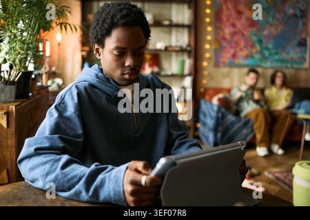 Afroamerikanischer Teenager, der am Tisch sitzt und sich auf Online-Lernen oder digitale Kommunikation zu Hause konzentriert. Nützlich für Bildung, Jugendtechnologie und Fernstudien Stockfoto