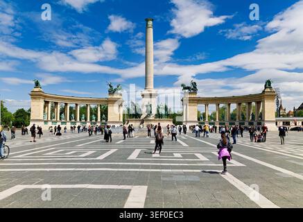 Die Leute versammeln sich auf dem Heldenplatz in Budapest. Auf dem Platz befinden sich Statuen und eine hohe Säule unter blauem Himmel. Besucher gehen zu Fuß und genießen die Gegend. Stockfoto