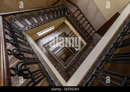 Blick auf die quadratische Spirale einer historischen Budapester Marmortreppe mit kunstvoller Eisenbalustrade - architektonisches Interieur Stockfoto