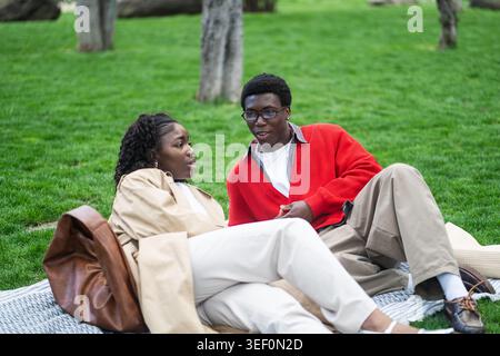 Positives afroamerikanisches Paar, Mann und Frau, die zusammen auf Karo im Stadtpark beim Picknick sitzen. Stockfoto