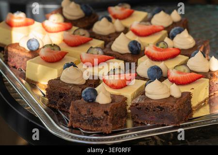 Gemischte Schokoladen-Brownies und cremige Mangobäcke mit frischen Erdbeeren, Heidelbeeren und Schlagsahne in warmem natürlichem Licht. Stockfoto