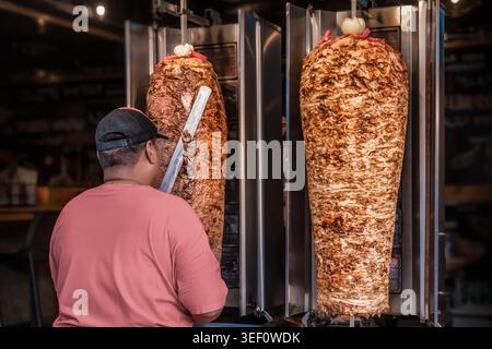 Restaurantarbeiter bereiten Shawarma und Döner auf vertikalem Grill in der Fast-Food-Küche zu. Das Bild zeigt das Schneiden von geröstetem Fleisch auf r Stockfoto