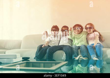 Kinder aus dem Nahen Osten sehen zu Hause gemeinsam einen Film mit 3D-Brille auf einem Sofa Stockfoto