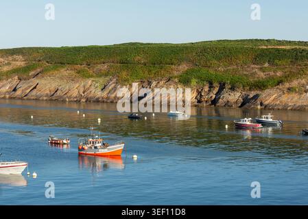 Blick auf kleine Boote in der Nähe von Kermorvan Point Le Conquet Finistere Bretagne France mit ruhigem blauem Wasser, felsiger Küste und grüner Vegetation u Stockfoto