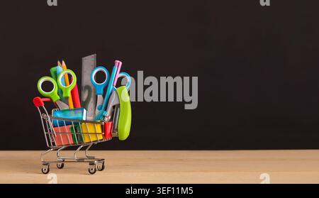 Shopping Cart mit Schulmaterial über schiefertafel Hintergrund Stockfoto