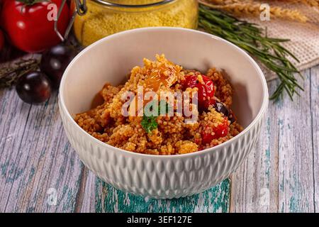 Nahaufnahme von köstlichem Couscous-Salat mit geröstetem Gemüse in weißer Keramikschale. Rustikales Ambiente mit Rohzutaten auf verwittertem blauen Holztisch Stockfoto