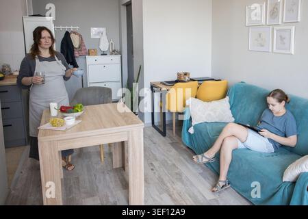 Glückliche Mutter, die den Tisch legt, während Ihr Kind lernt und pc-Tablet-Geräte zu Hause verwendet Stockfoto
