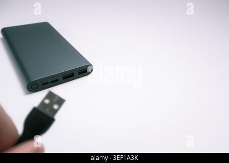 USB-Kabel von Hand an die Powerbank anschließen. USB-Kabel mit Handhalterung und graue Powerbank. Stromspargerät Powerbank für Smartphone. Stockfoto