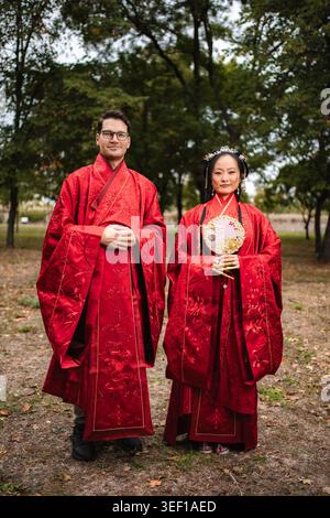 Interkulturelles Paar in roter traditioneller chinesischer Hochzeitskleidung Stockfoto