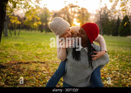 Verschiedene Freundinnen genießen Huckepack-Fahrt im Herbstpark Stockfoto
