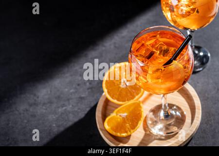 Nahaufnahme von zwei Aperol Spritz Cocktails, serviert mit Eiswürfeln, Orangenscheiben und schwarzen Strohhalmen in eleganten Stängelgläsern. Hellorangefarbener Sommer-Aperitif Stockfoto