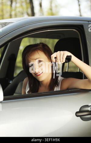 Junge Frauen lächeln und sitzen im Auto. Brünette hält, Schlüssel zeigt Stockfoto