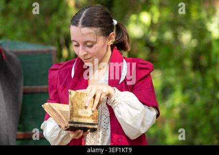 Junge Frau im historischen Kostüm liest draußen ein altes Buch Stockfoto