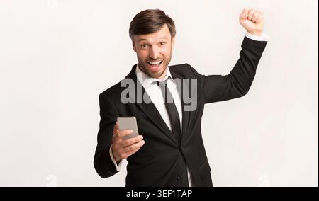 Aufgeregter Mann im Anzug, der Erfolg feiert, während er das Smartphone hält Stockfoto
